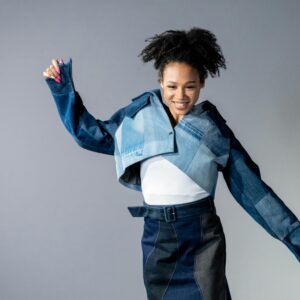 Joyful model with afro hair in a trendy denim ensemble. Studio setup.